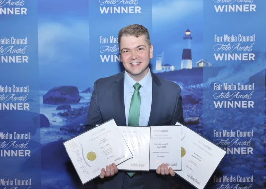 A man holding four awards in front of a blue background.